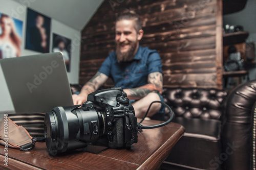 Beautiful smiling portrait of the photographer at the workplace. The concept of the creative process, skill and favorite pastime. Male boss sitting on the couch in his office, working on laptop