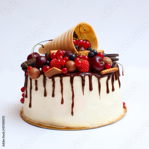 cake with white chocolate cream and decorated with berries and cookies on white background