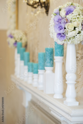 Floral arrangement with white and blue flowers and candles on candle holders. Wedding decor idea. 