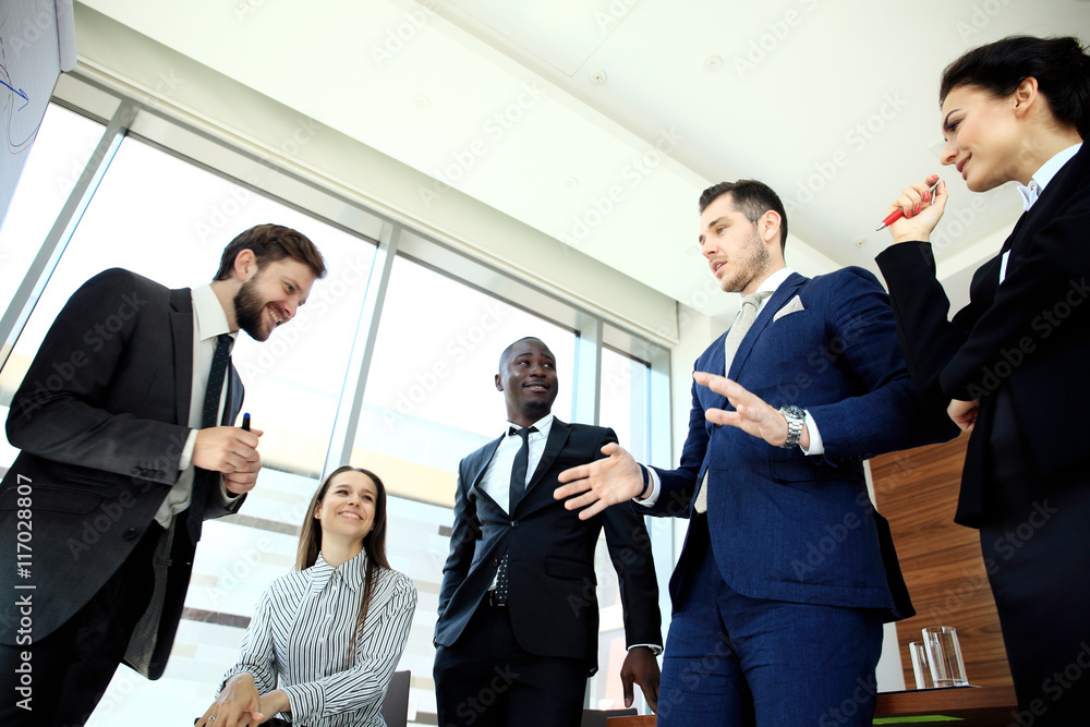 Young handsome man gesturing and discussing something while his coworkers listening to him at the office Young handsome man gesturing and discussing something while his coworkers listening to him at the office