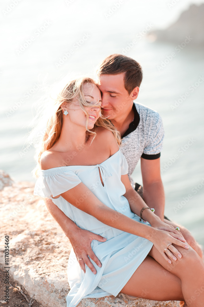 Smiling girl sitting with man on rock over sea. Romantic date. Smiling girl sitting with man on rock over sea. Romantic date.