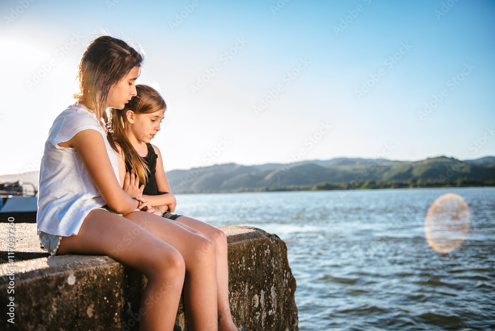Girl comforting her sad friend on dock Girl comforting her sad friend on dock