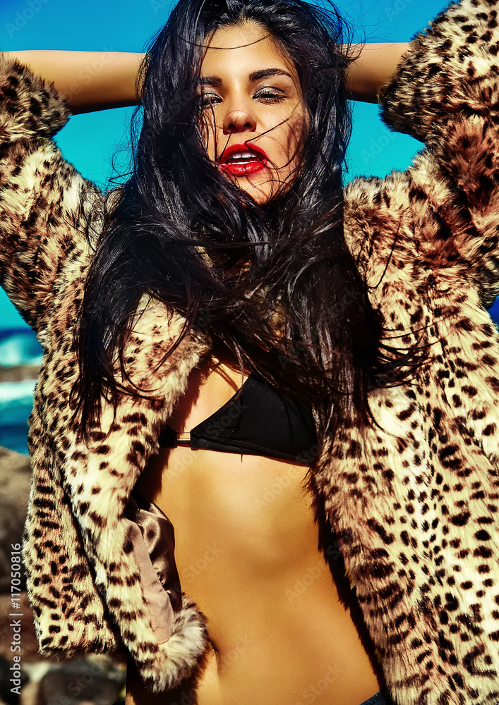 High fashion look.glamor sexy sunbathed Caucasian model girl in leopard fur  coat posing behind blue beach ocean water in vogue style Stock Photo