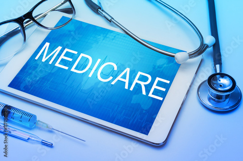 Medicare word on tablet screen with medical equipment on background photo