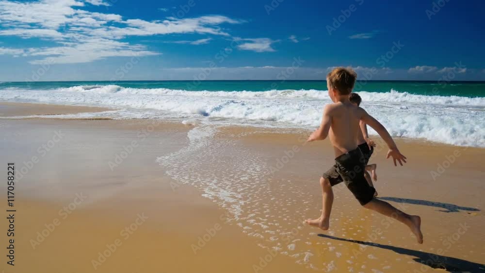 Two little boys running on a sandy vibrant beach on sunny day Two little boys running on a sandy vibrant beach on sunny day
