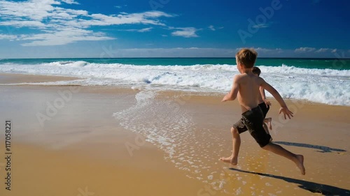 Two little boys running on a sandy vibrant beach on sunny day