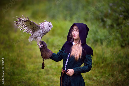 girl in medieval dress is holding an owl on her arm