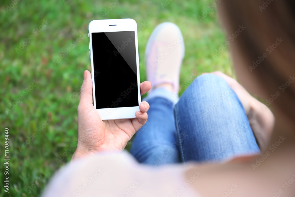 Woman holding smartphone on blurred grass background