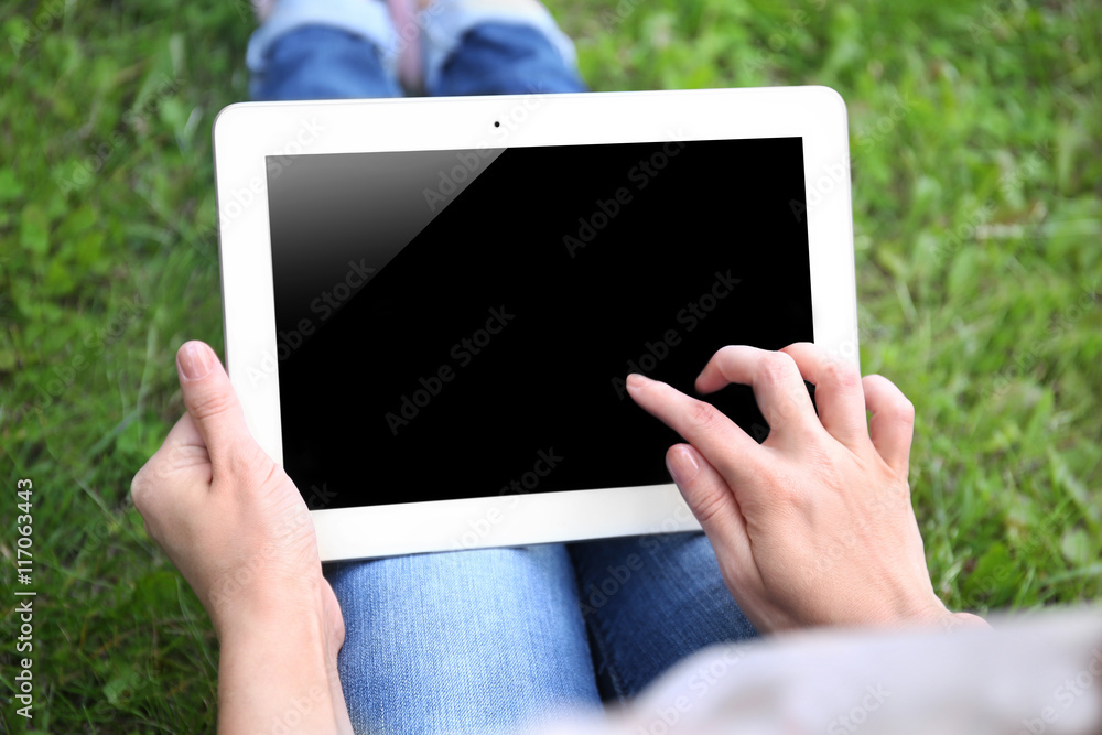 Woman holding tablet on blurred grass