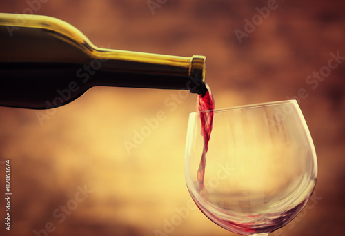 Red wine pouring in glass on brown background