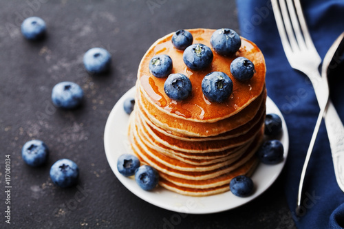 Stack of baked american pancakes or fritters with blueberries and honey syrup on rustic black background. Delicious dessert for breakfast.