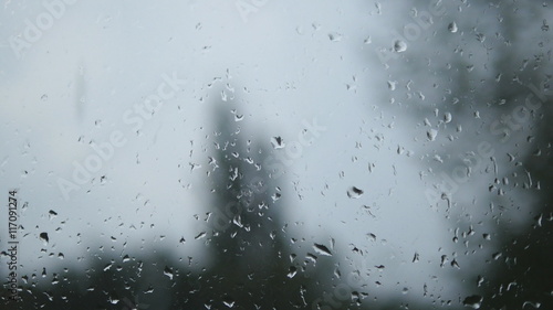 Close-up of water droplets on glass. Rain drops on window glass with blur background. Blurred tree and sky. Rainy days, rain running down window, bokeh