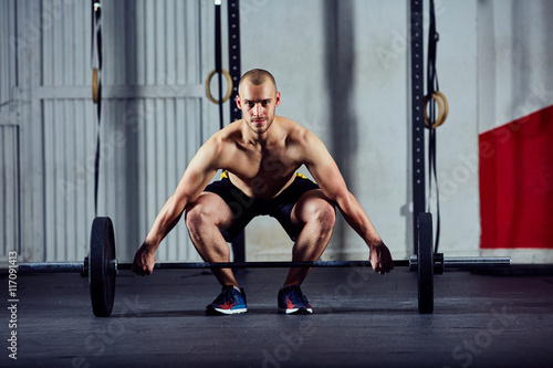 Young athletic man doing weightlifting workout with barbell at t