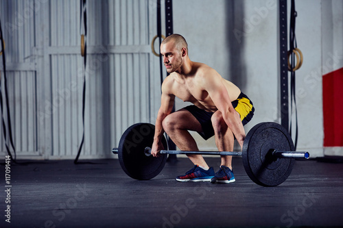 Young athlete doing weightlifting workout with barbell at the gy