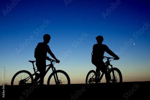 Two cyclists on the background of night sky and moon