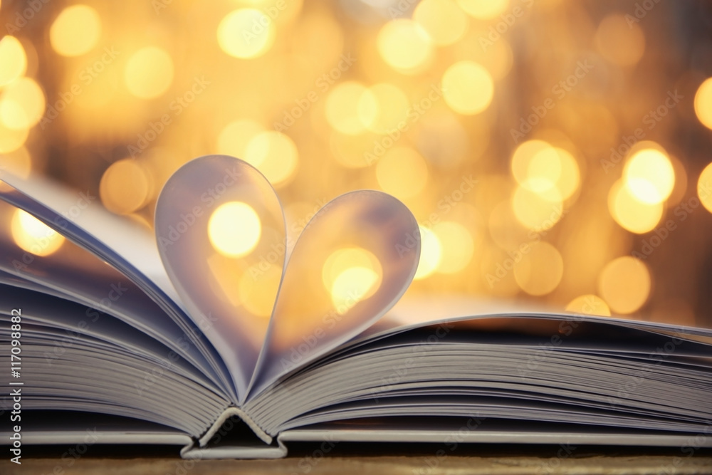 Sheets of book curved into heart shape on wooden table against unfocused lights Sheets of book curved into heart shape on wooden table against unfocused lights