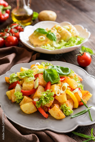 Fried potato salad with lettuce, pepper, onion and baked fish fillets covered with cheese photo