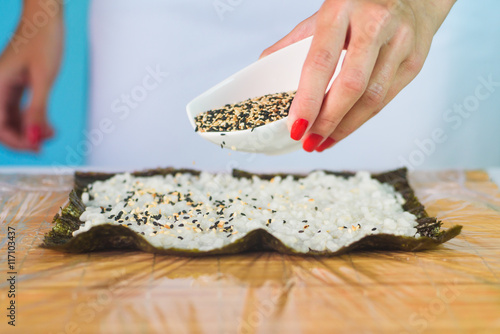 Hands of woman chef filling japanese sushi rolls with rice and sesame on a nori seaweed sheet.