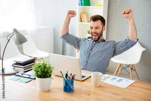 Happy man completed task and triumphing with raised hands photo