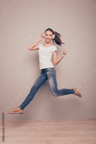 Full length portrait of a happy woman jumping while listening mu