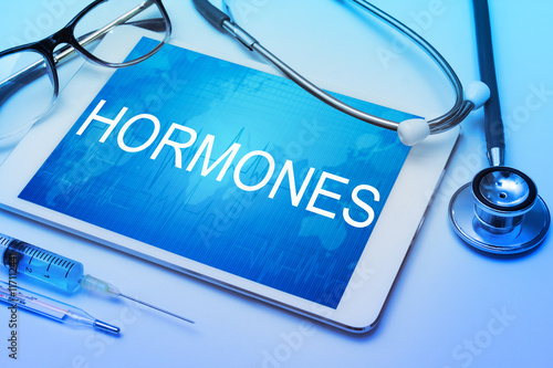 Hormones word on tablet screen with medical equipment on background