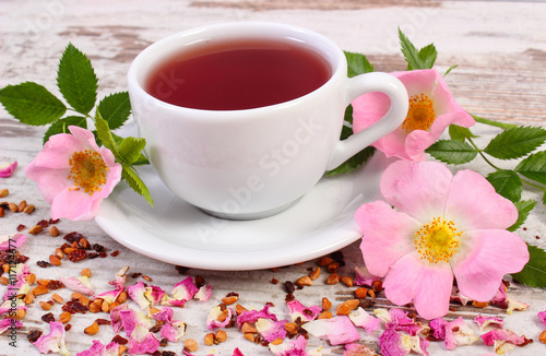 Cup of tea with wild rose flower on old rustic wooden background