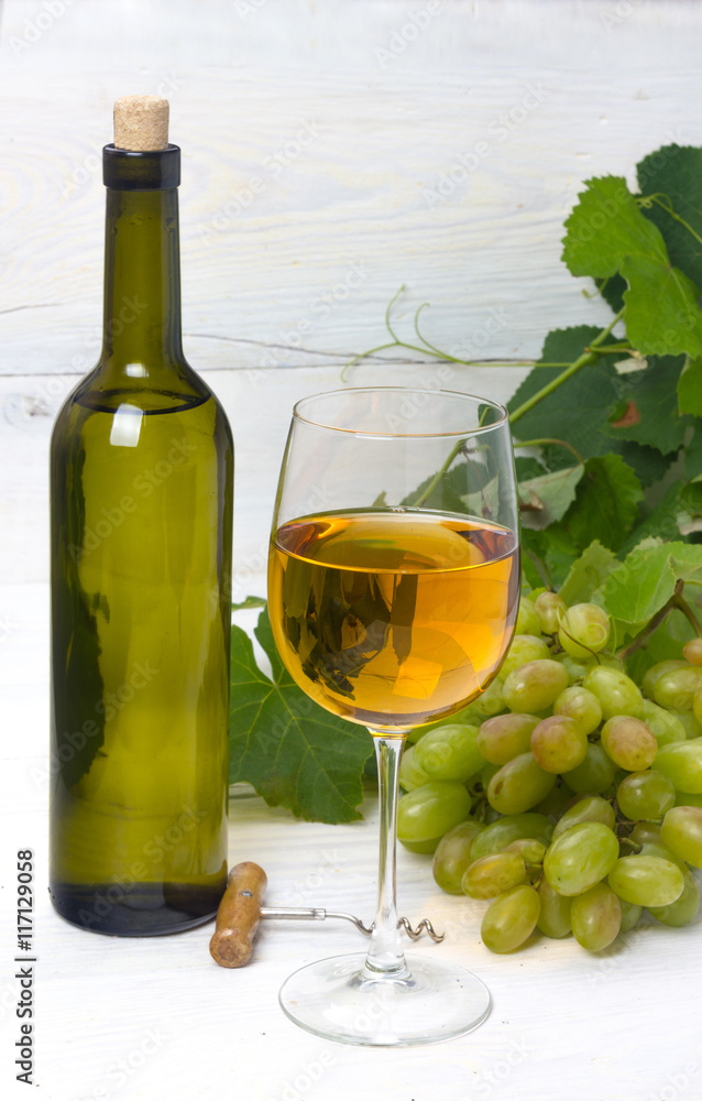 glass and bottle of white wine with grapes on a wooden table