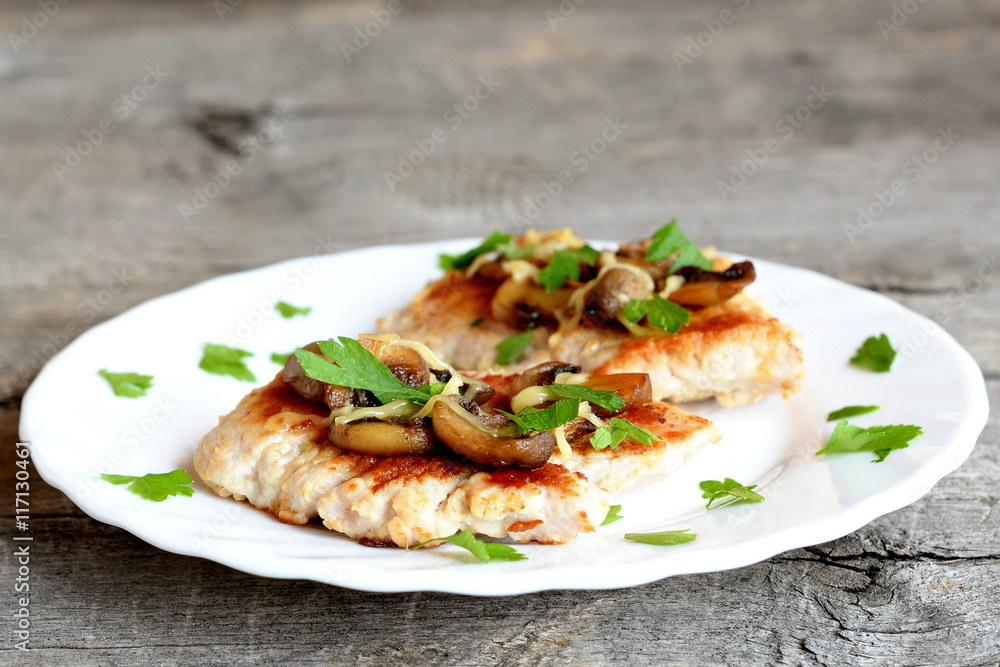 Roasted Turkey fillet with cheese and agaricus on a plate and on old wooden background. Delicious Turkey steaks garnish with fresh parsley. Closeup Roasted Turkey fillet with cheese and agaricus on a plate and on old wooden background. Delicious Turkey steaks garnish with fresh parsley. Closeup