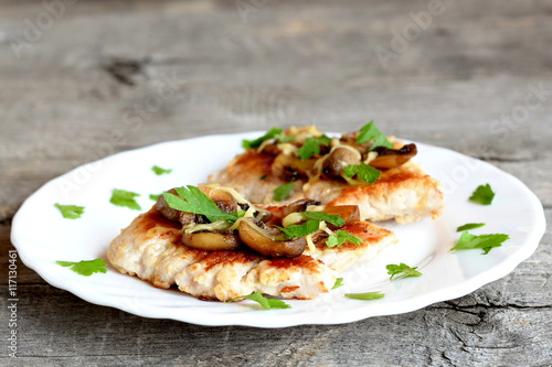 Roasted Turkey fillet with cheese and agaricus on a plate and on old wooden background. Delicious Turkey steaks garnish with fresh parsley. Closeup