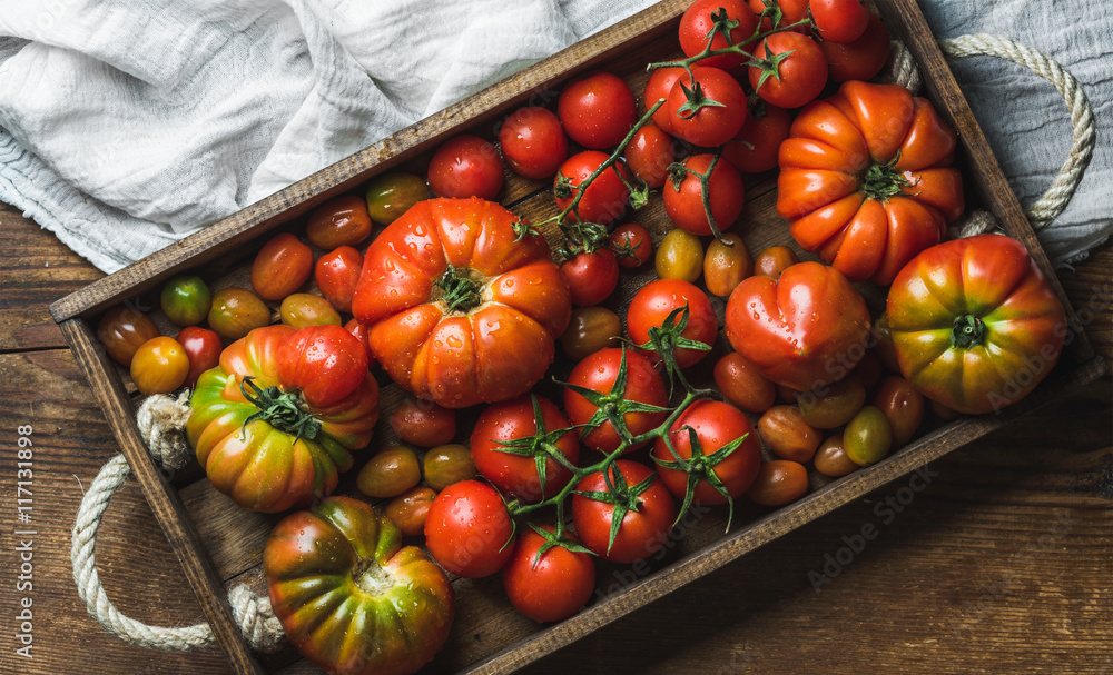 Colorful tomatoes of different sizes and kinds in dark wooden tray over ...