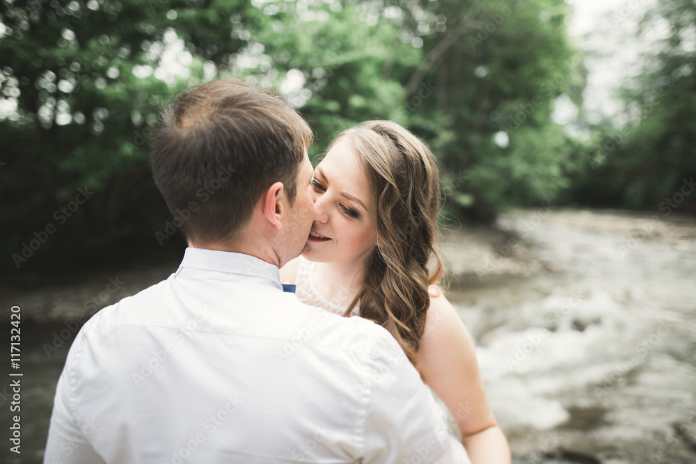 elegant stylish happy brunette bride and gorgeous groom on the background of a beautiful waterfall in the mountains