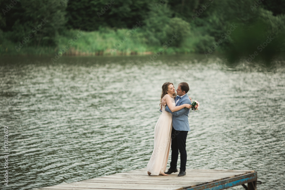 Beautiful wedding couple, bride,groom kissing and posing on the bridge near lake