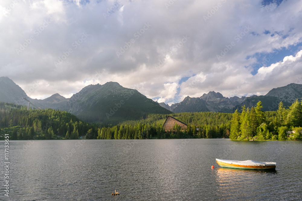 Obraz premium Peaceful mountain scene with mountain hotel next to a lake with boat. Scenic view of Strbske Pleso, High Tatras National Park, Slovakia.