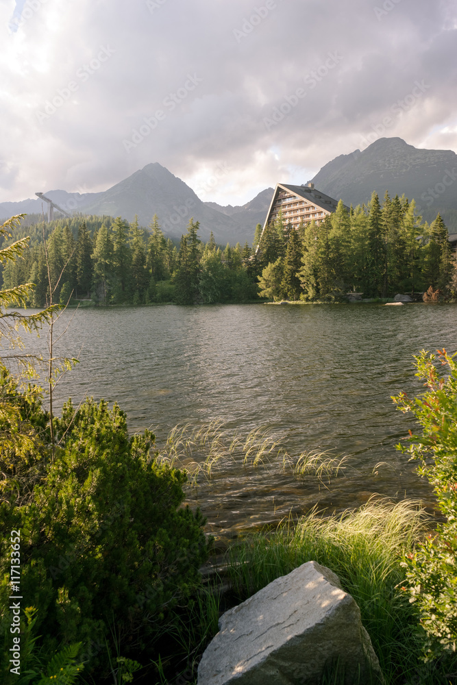 Obraz premium Vertical view of beautiful mountain landscape with hotel next to a lake. Strbske Pleso Town in High Tatras National Park, Slovakia.