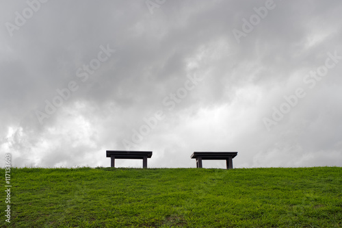 Two benches in the center of green field with dark cloudy sky 