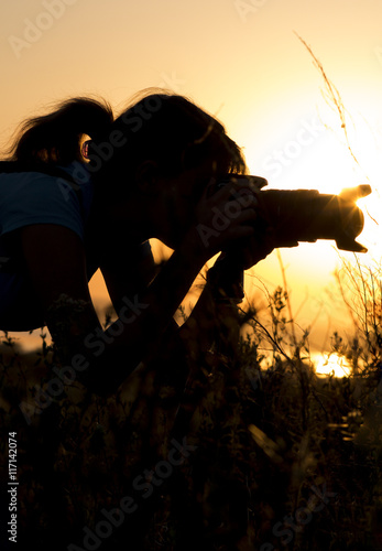 silhouette portrait of a young woman photographing a beautiful nature at sunset on photo equipment