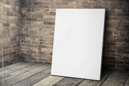 Obraz na plátně Blank white canvas frame leaning at grunge brick wall and wood f