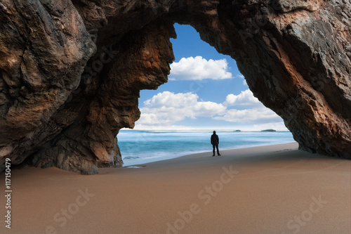Lonely man at the rocky arch watching cloudy sky