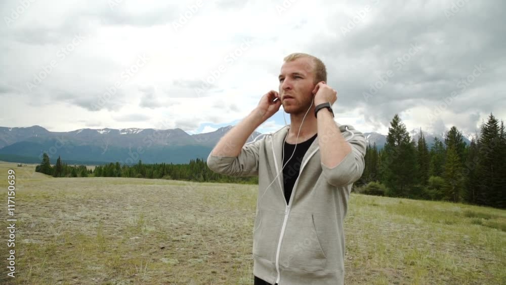 Mature male runner having a rest after jog while listening to music in headphones and sitting on mountain rock Mature male runner having a rest after jog while listening to music in headphones and sitting on mountain rock