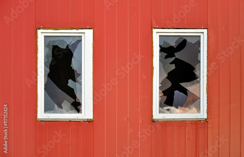 Abandoned industrial building. Red wall of sandwich-panels and two windows with broken glass