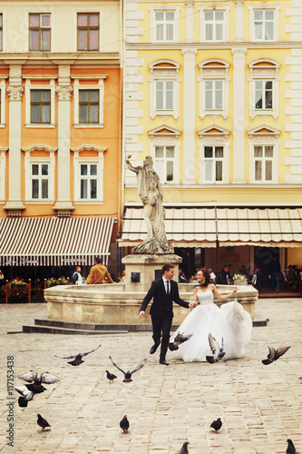 Married couple run across the citysquare full of pigeons