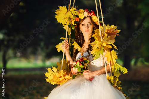 Autumn sun shines over s stunning bride while she sits on a swin photo