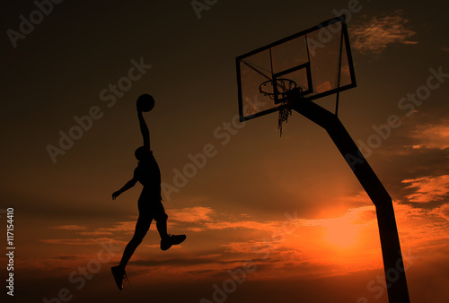 Young man is playing basketball during sunset