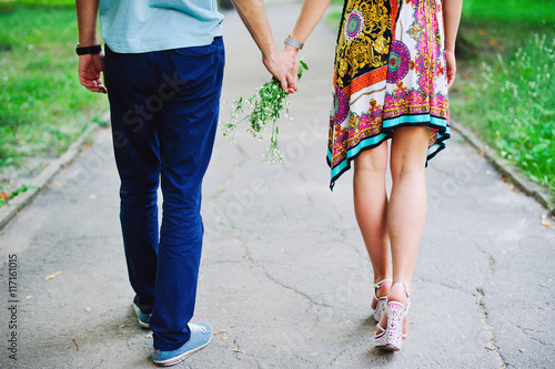 Young couple walking together through the park holding hands, rear view