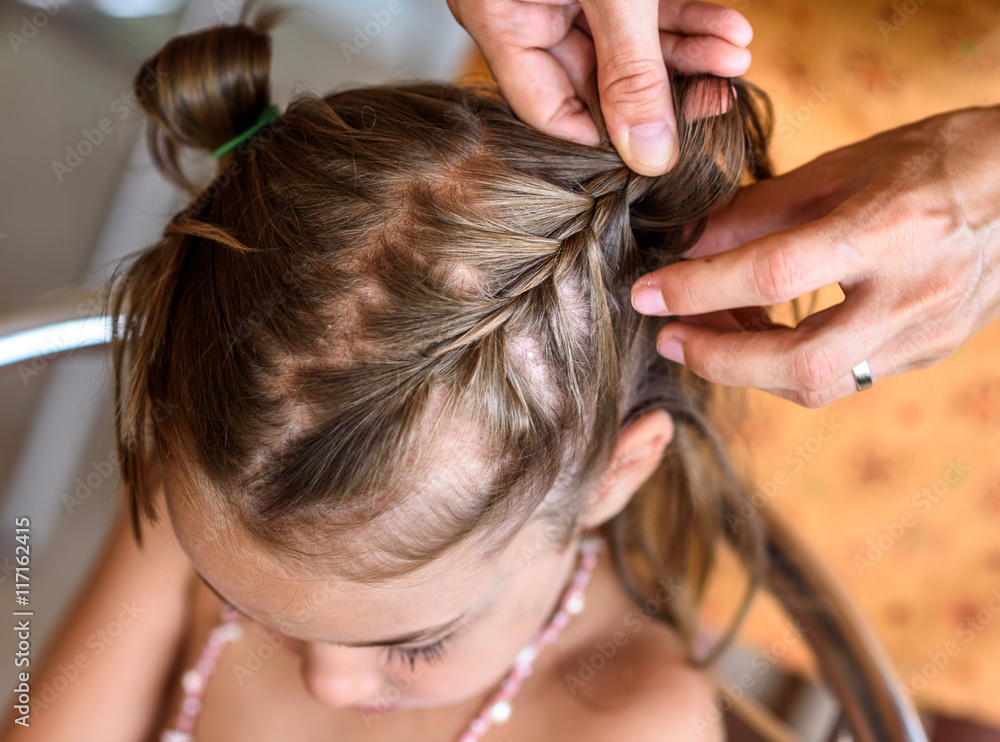Fototapeta premium Mother is making of braids on little daughter's head.