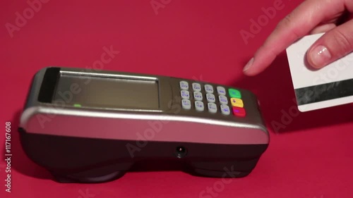 Hand dialing pin code on pin pad of pos terminal and swipe credit card on red background