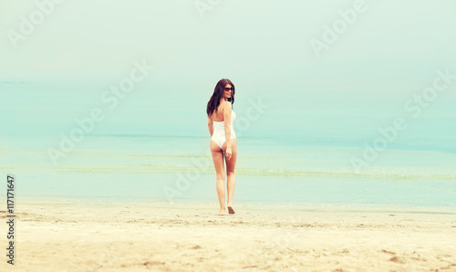 young woman in swimsuit walking on beach