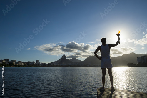 Silhouette of torchbearer athlete standing with sport torch against the setting sun of the Rio de Janeiro Brazil skyline at Lagoa Rodrigo de Freitas lagoon photo