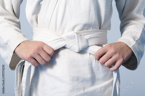 Teenage's hands tightening white belt on a kimono