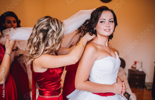 Bride and three bridesmaids in similar red dresses with perfect make up and hair style in a light loft space